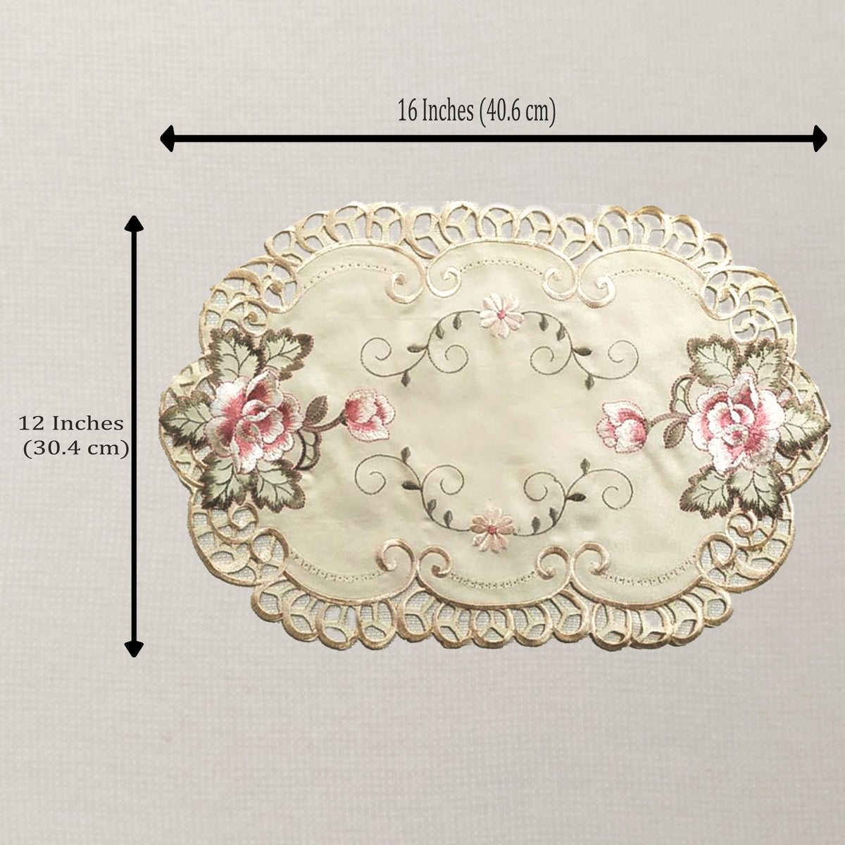 An oval embroidered placemat with a scalloped lace-like border, pink floral motifs, and gray-green leaves on a cream background. Black measurement arrows and text indicate dimensions of 16 inches by 12 inches.