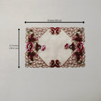An embroidered lace table mat with a cream center and pink floral motifs, shown with black dimension lines indicating 16 inches by 12 inches.