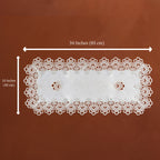 White rectangular lace doily with scalloped edges and two small floral cutouts, shown on a brown background with dimension arrows indicating 34 inches by 16 inches.
