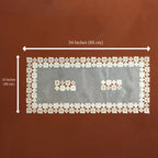 A rectangular white lace textile with embroidered floral borders and two small embroidered motifs in the center, shown on a brown background with dimension arrows and text indicating 34 inches by 16 inches.
