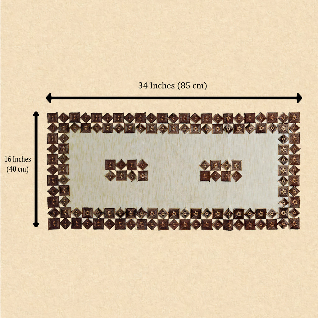 A rectangular patchwork table runner made of many small brown and cream fabric squares, shown on a beige background with measurement arrows labeling it 34 inches by 16 inches.