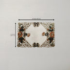A rectangular placemat with a white center and ornate floral lace-like border, shown on a light neutral background with dimension arrows indicating 16 inches by 12 inches.
