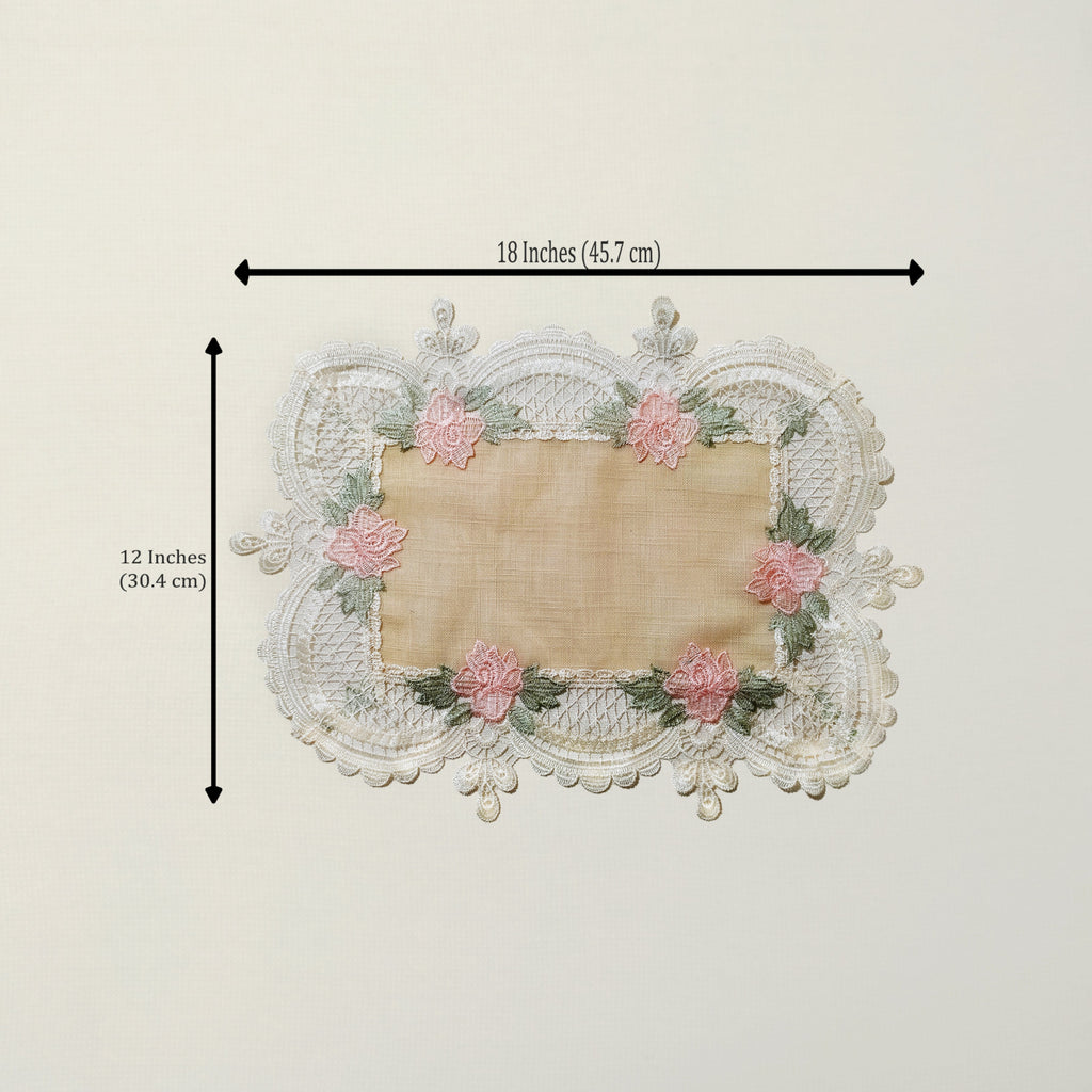 A rectangular lace doily with a beige center and pink floral embroidery around the border, shown with black dimension arrows and text indicating 18 inches by 12 inches.