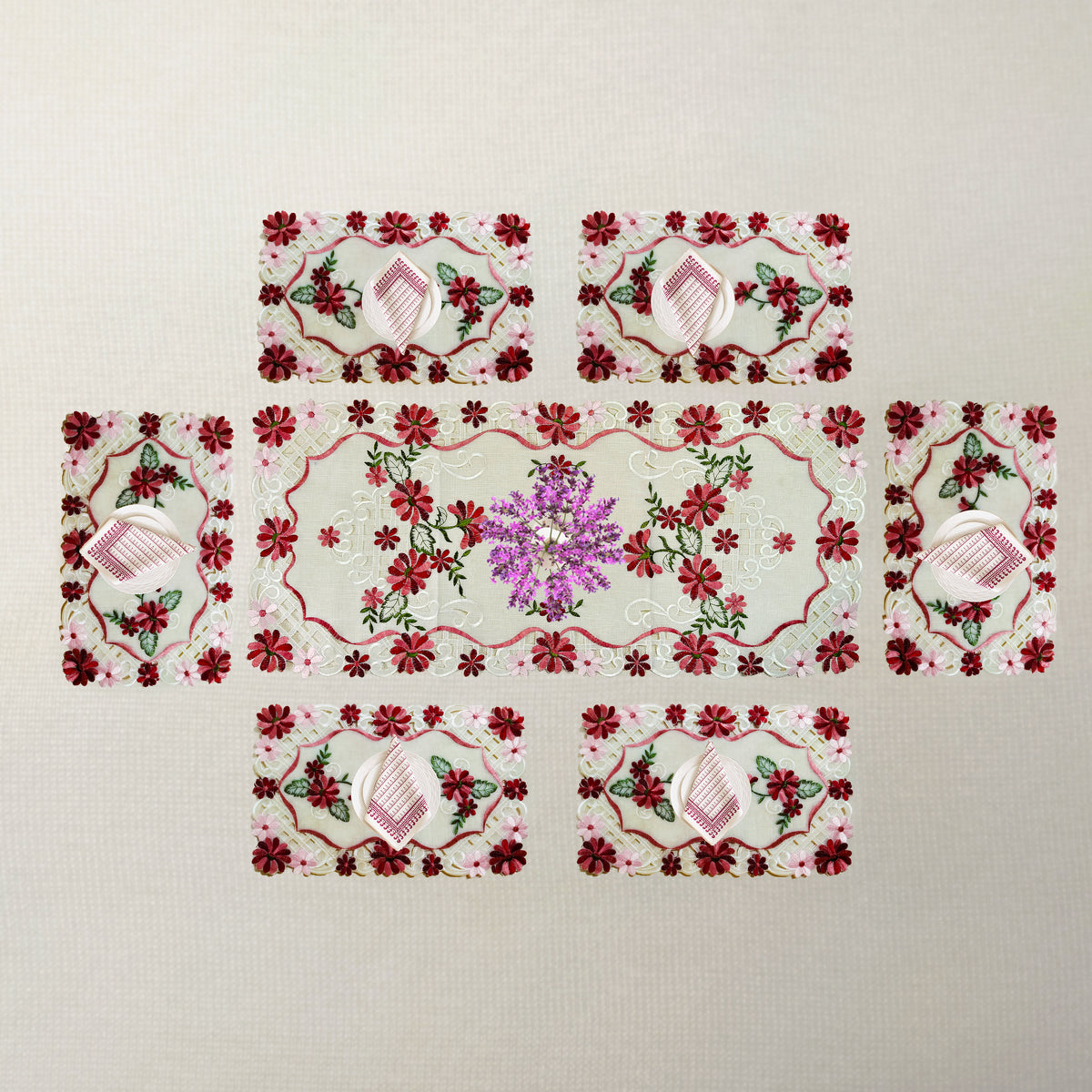 A set of six rectangular embroidered patches arranged in a cross-like layout on a light beige textured fabric background. The central patch is larger and features a purple floral motif, while the surrounding five patches are smaller and decorated with red and pink floral patterns, pink striped hearts, and green leaves.